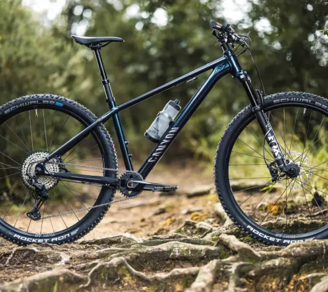 Muscle bike Canyon blu scuro su sentiero sterrato con radici affioranti.