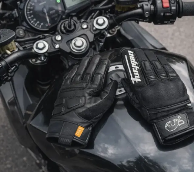 Guanti da moto neri posati sul serbatoio di una moto. Non esistono guanti ad uso motociclistico di tipo omologato, ma questi sembrano pronti per ogni avventura.