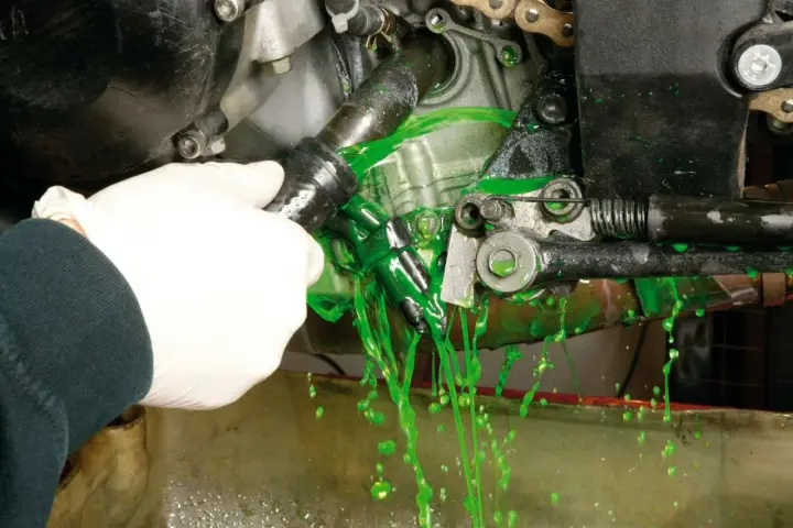 Mano con guanto bianco che scollega un tubo, facendo fuoriuscire liquido verde brillante per il cambio del liquido radiatore.