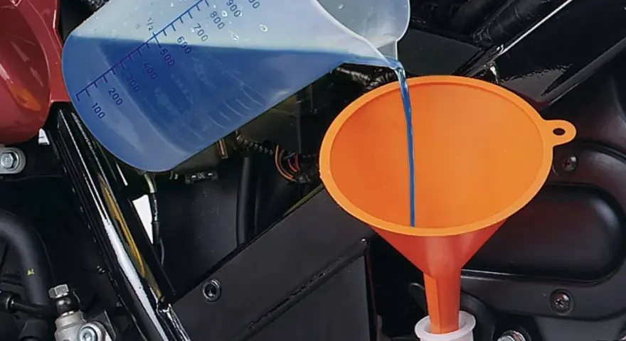 Versando liquido refrigerante blu in un imbuto arancione per diluirlo.