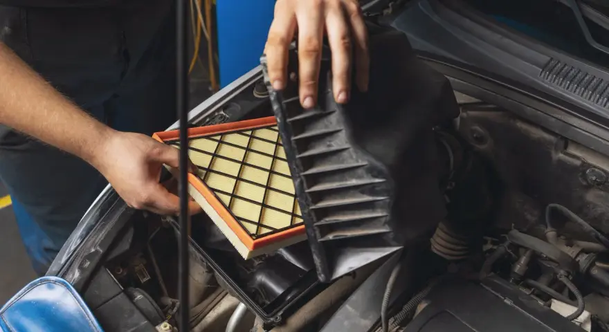 Mani che sostituiscono un filtro aria sporco nel vano motore di un'auto.
