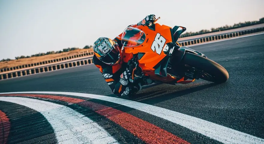 Un pilota con tuta arancione e casco decorato piega in curva su una KTM su una pista da corsa.