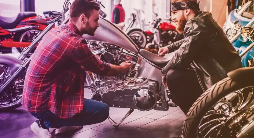 Due uomini esaminano un motore di moto custom. Uno mostra all'altro i dettagli, forse discutendo il costo della messa in strada della moto.
