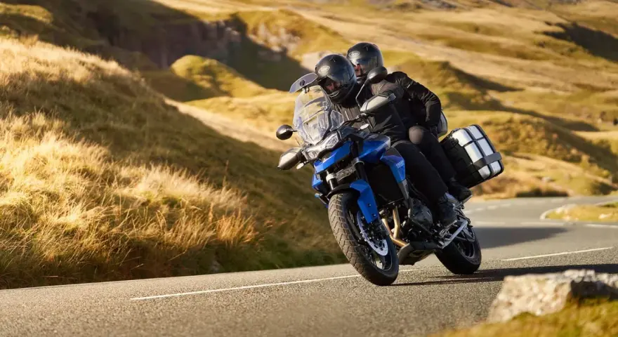 Coppia su una moto per due persone sfreccia su una strada panoramica tra colline dorate.