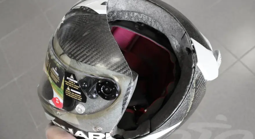 Casco da moto con calotta in fibra di carbonio e abs o policarbonato, visiera trasparente e interni rossi. La calotta presenta una crepa.