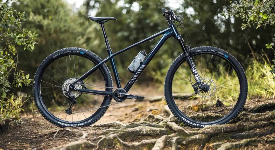 Muscle bike Canyon blu scuro su sentiero sterrato con radici affioranti.