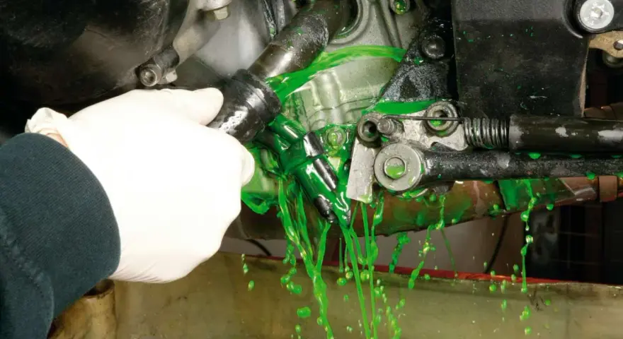 Mano con guanto bianco che scollega un tubo, facendo fuoriuscire liquido verde brillante per il cambio del liquido radiatore.