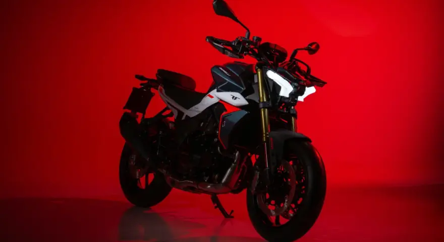 La Benelli TNT 500, con il suo design aggressivo e i fari a LED luminosi, si staglia su uno sfondo rosso acceso, pronta a conquistare la strada.