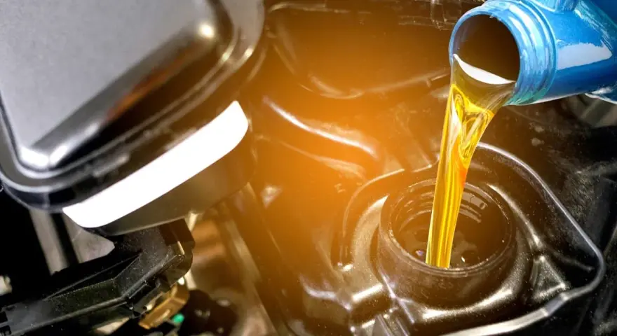 Olio giallo versato da una bottiglia blu in un motore. La differenza tra olio sintetico e minerale è fondamentale per la salute del motore.