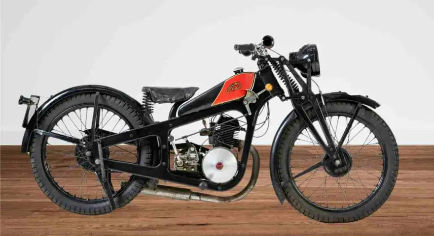 Una rara moto d'epoca, nera con serbatoio rosso e logo, su un pavimento di legno.