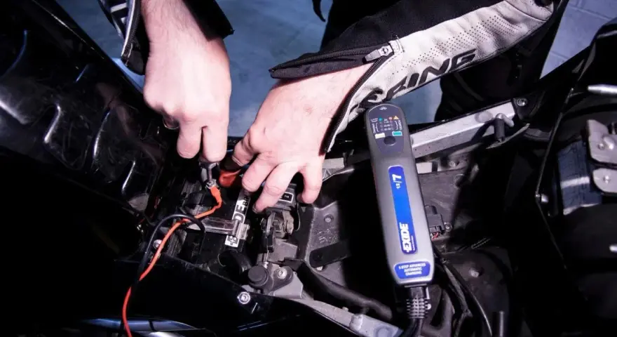 Mani che collegano un caricabatterie Exide a una batteria di moto. La batteria non tiene la carica, quindi si prova a ricaricarla.