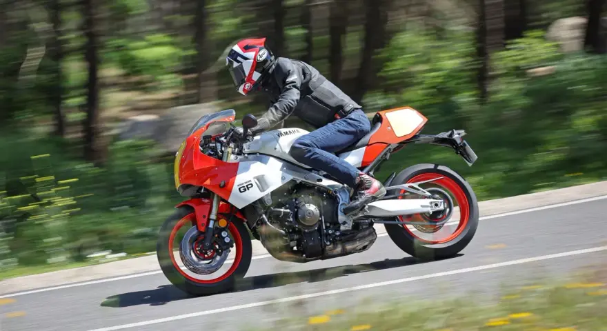 Un motociclista sfreccia su una Yamaha XSR900 GP, con il paesaggio sfocato dallo sfondo verde e giallo.