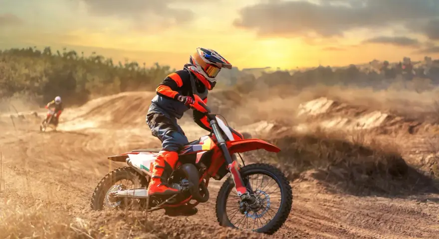Un pilota di **enduro motocross** sfreccia su un terreno polveroso al tramonto, sollevando terra.