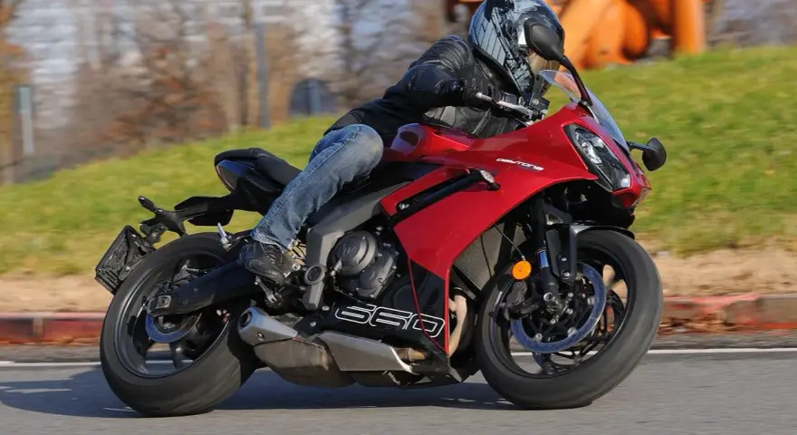 Un motociclista sfreccia su una moto sportiva rossa, tra le migliori moto sportive, con un casco moderno e jeans.