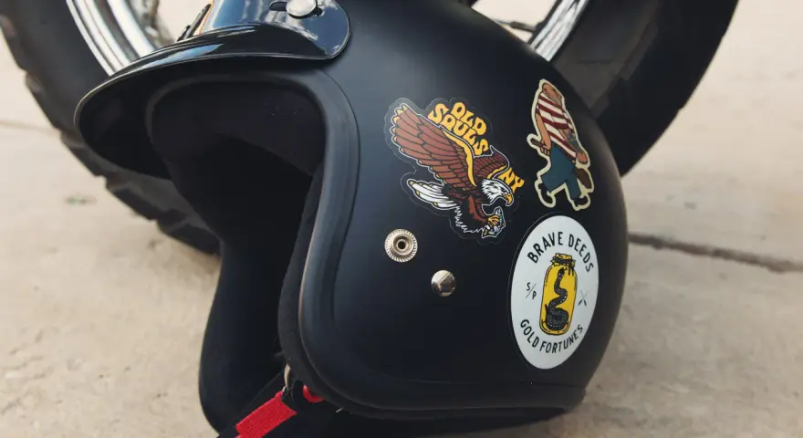 Casco nero con adesivi: un'aquila, un personaggio a strisce e un serpente in un barattolo. Si possono attaccare adesivi sul casco per personalizzarlo.