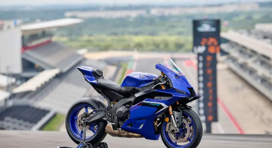 Yamaha R9, blu, su un cavalletto, con sfondo di un circuito. Dettagli tecnici da scoprire.