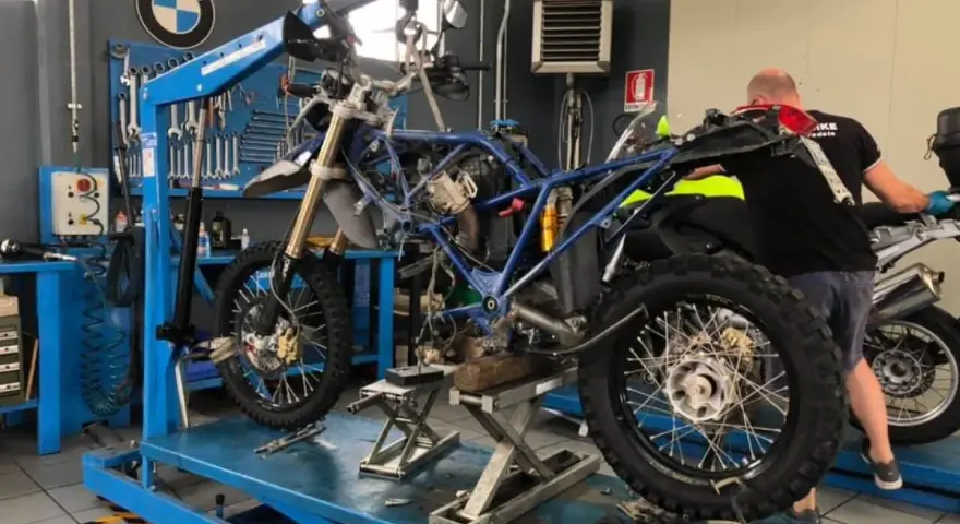 Officina BMW: moto smontata su sollevatore, in attesa del raffreddamento motore. Attrezzi e meccanico al lavoro.