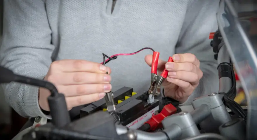Mani che collegano i cavi a una batteria da moto ferma per ricaricarla.