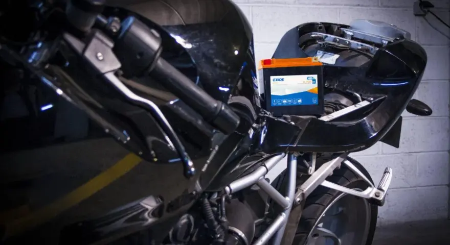 Una batteria nuova va caricata. La nuova batteria Exide è posizionata sul telaio di una moto nera lucida, pronta per essere collegata.