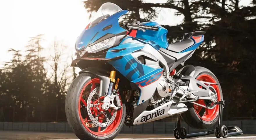 Aprilia carenata blu e rossa, con cerchi rossi, pronta per sfrecciare su pista.