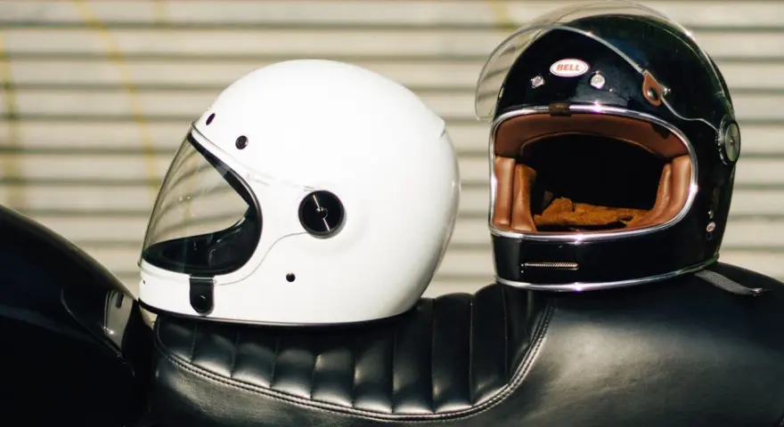 Due caschi integrali, uno bianco e uno nero, appoggiati sul sedile di una moto. Il peso del casco integrale è un fattore importante per il comfort.