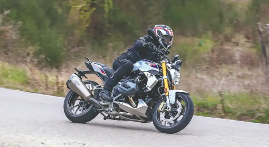 Motociclista in sella a una BMW R 1250 R, affronta una curva. Nessun difetto visibile in questa immagine.
