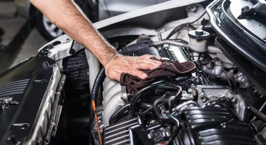 Mano che pulisce il motore dell'auto con un panno scuro, parte di un lavaggio motore accurato.