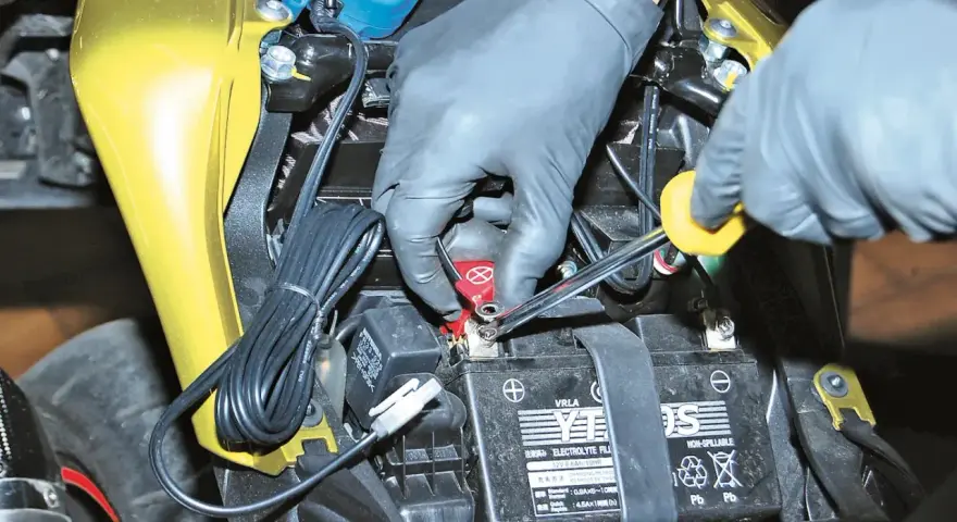 Mani guantate collegano un mantenitore di carica moto sempre collegato alla batteria.