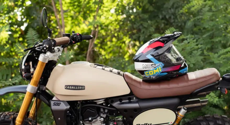Casco colorato appoggiato su una moto Caballero Rally color crema. Perfetta per avventure, queste moto facili da guidare ti portano ovunque.