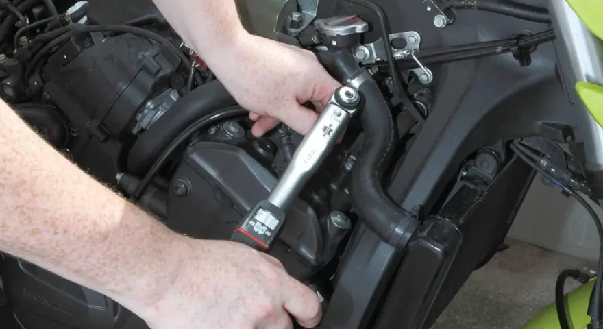 Mani che usano una chiave dinamometrica per il cambio candele di una moto.
