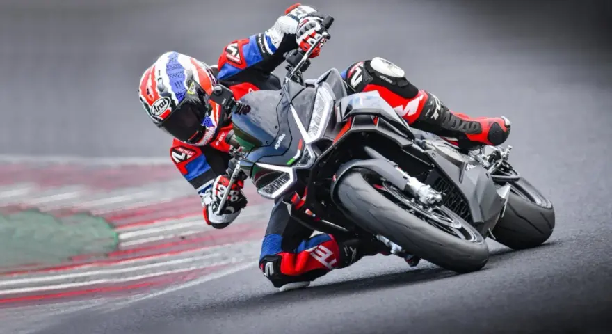Un pilota in piega su una Aprilia Tuono 660 Factory, con tuta rossa e blu, affronta una curva su pista.