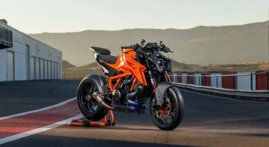 KTM 1290 Duke arancione su un cavalletto, pronta per sfrecciare su un circuito al tramonto.