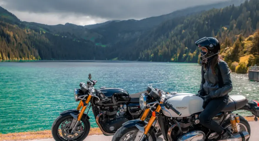 Due moto da enduro, una nera e una bianca, con una donna in sella, godono del panorama di un lago alpino.