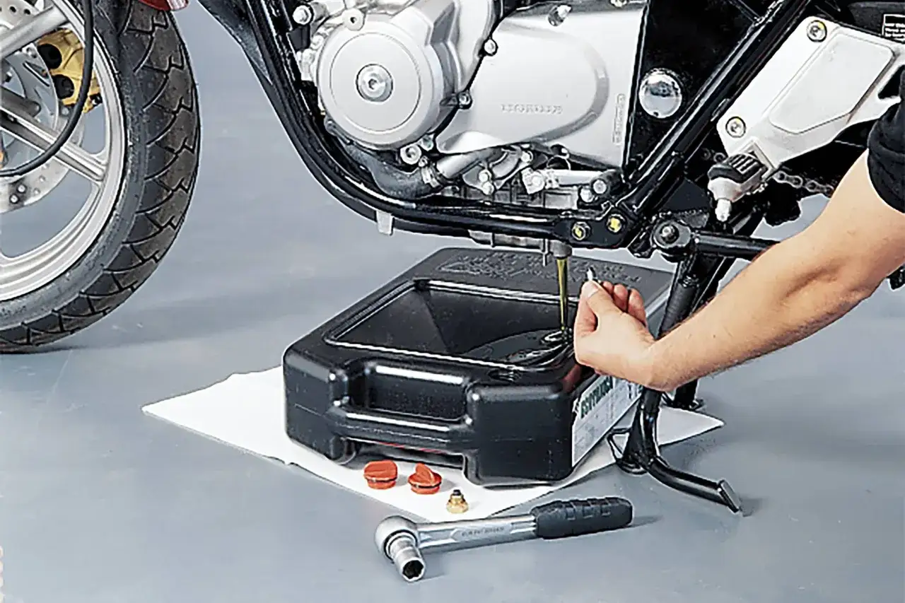 Cambio olio moto: un tecnico svuota l'olio esausto per ridurre il consumo di olio motore e mantenere il motore in salute.