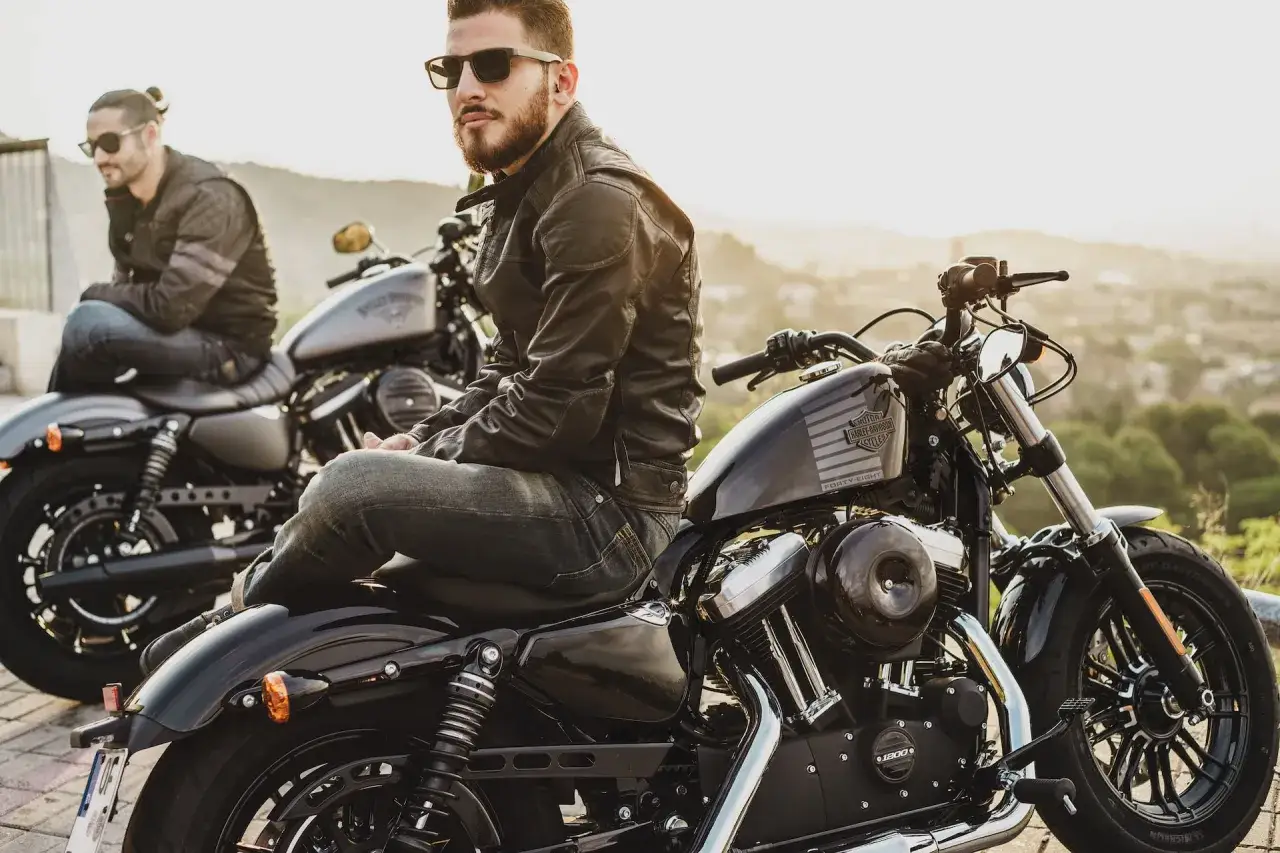 Due uomini con giacche di pelle e jeans, pronti a partire in moto. Ecco come vestirsi per andare in moto con stile e sicurezza.