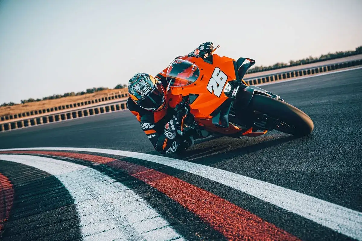 Un pilota con tuta arancione e casco decorato piega in curva su una KTM su una pista da corsa.