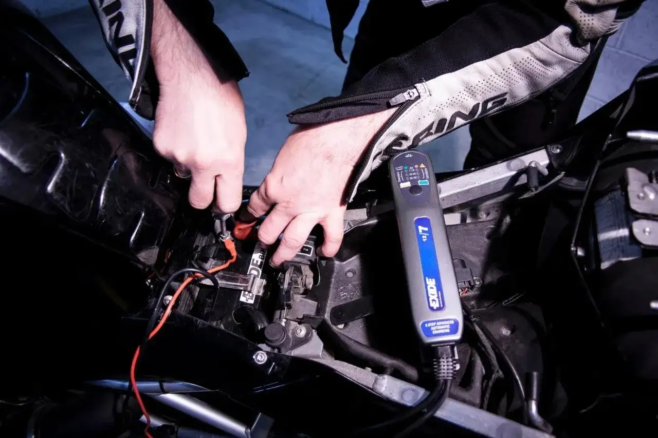 Mani che collegano un caricabatteria Exide alla batteria di una moto, mostrando come caricare batteria moto senza caricabatteria.