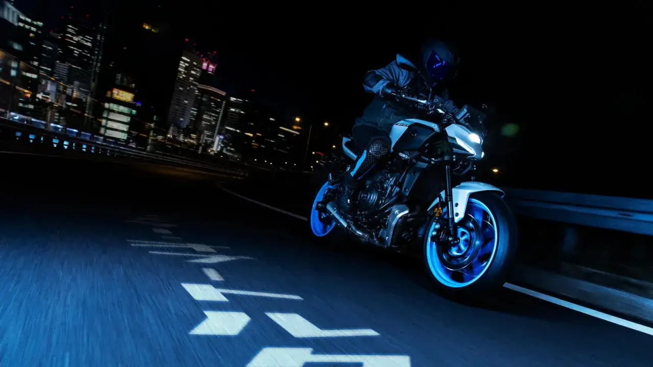 Una Yamaha scarenata sfreccia di notte in città, con luci al neon che illuminano la strada e la moto.