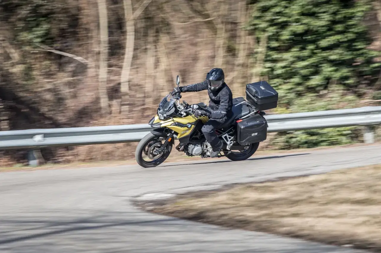 Motociclista su moto da turismo gialla con borse laterali e bauletto, in movimento su strada. La differenza tra moto e scooter è evidente nella posizione di guida e nel design.