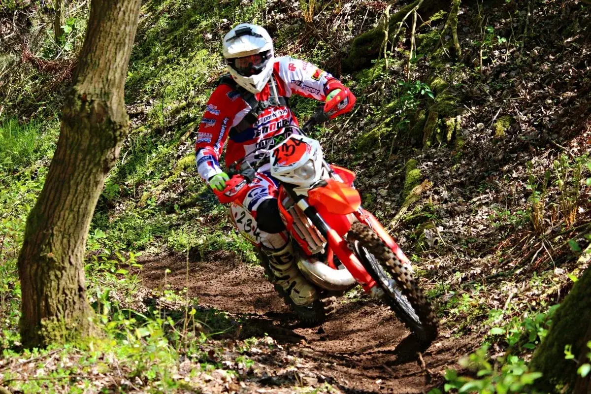Un pilota esperto sfreccia su una moto da cross arancione, affrontando un sentiero fangoso nel bosco. Sembra la miglior moto da montagna per un'avventura così emozionante.