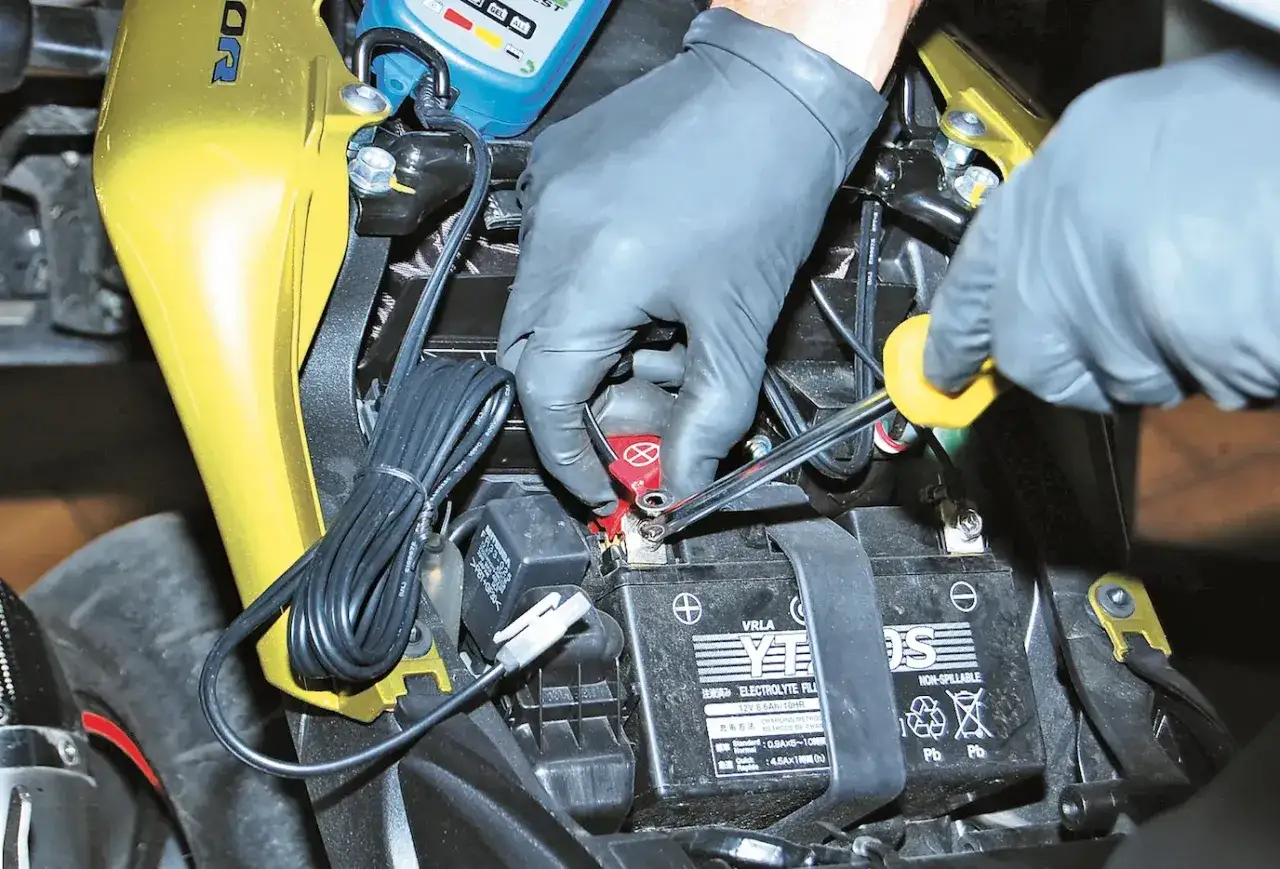 Mani guantate stringono il polo della batteria moto, un'operazione delicata: una batteria sempre in carica si rovina.
