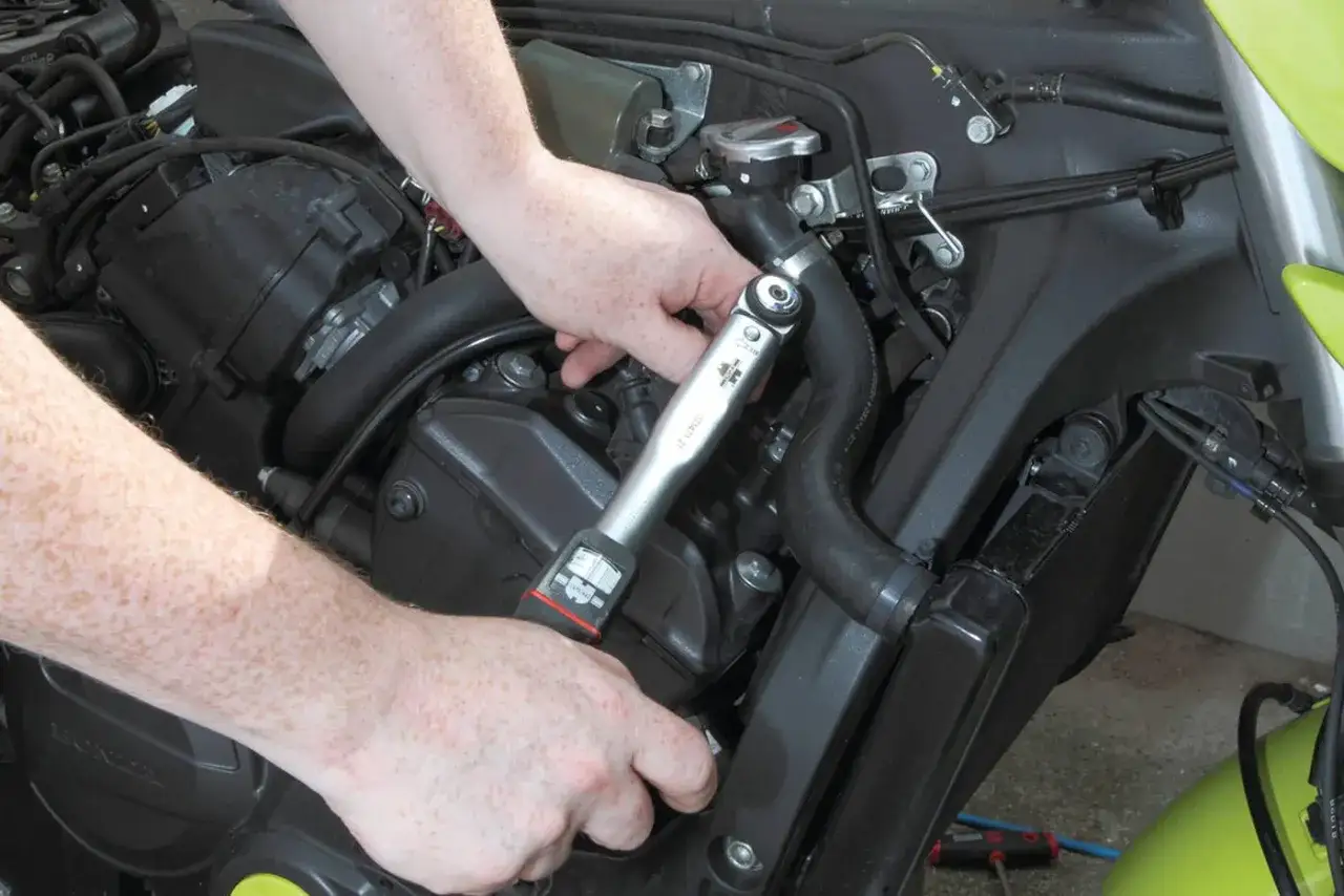Mani che usano una chiave dinamometrica per il cambio candele di una moto.