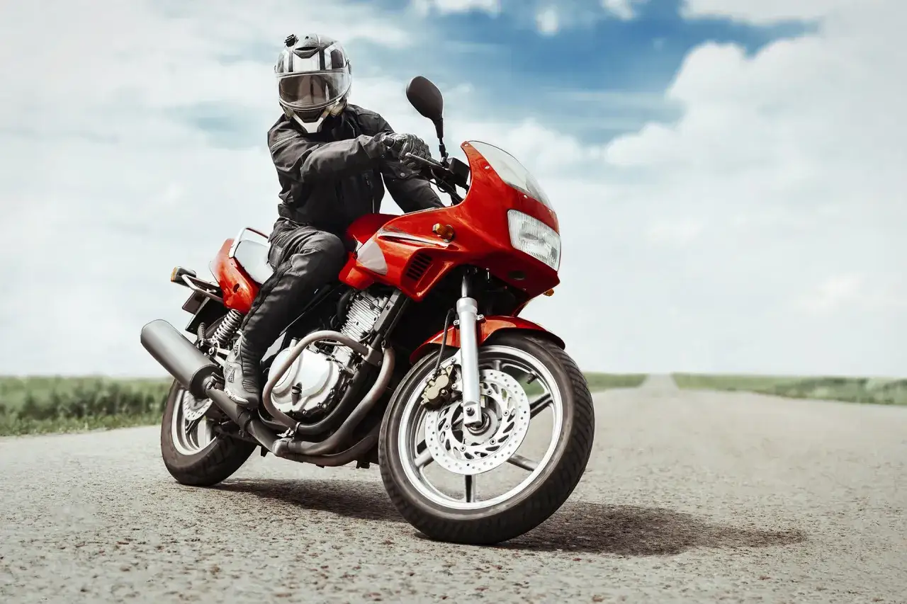 Motociclista su una moto rossa, un vero roadster, simbolo di libertà e avventura su strada.
