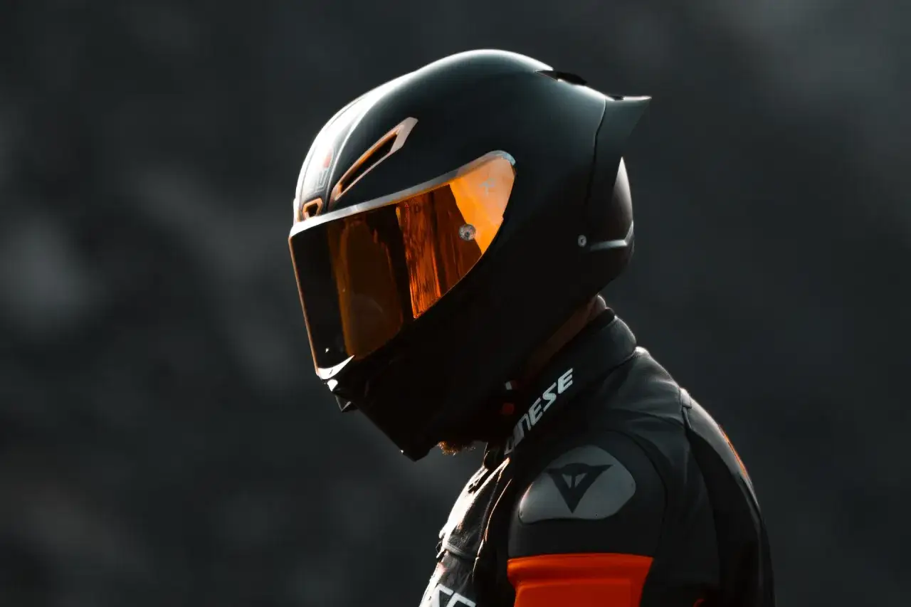 Motociclista con casco nero e visiera arancione riflettente, simbolo di caschi più sicuri per la protezione in pista.