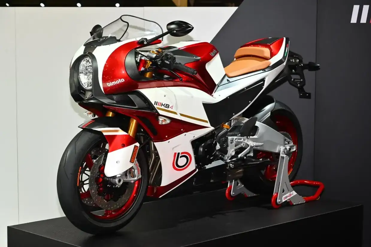 La Bimota KB4, una moto sportiva con carenatura rossa e bianca, sella color cuoio e dettagli dorati, esposta su un piedistallo.