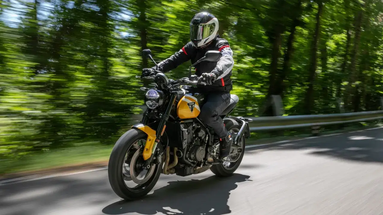 Motociclista alto 1.90 sfreccia su una moto gialla tra alberi verdi sfocati.