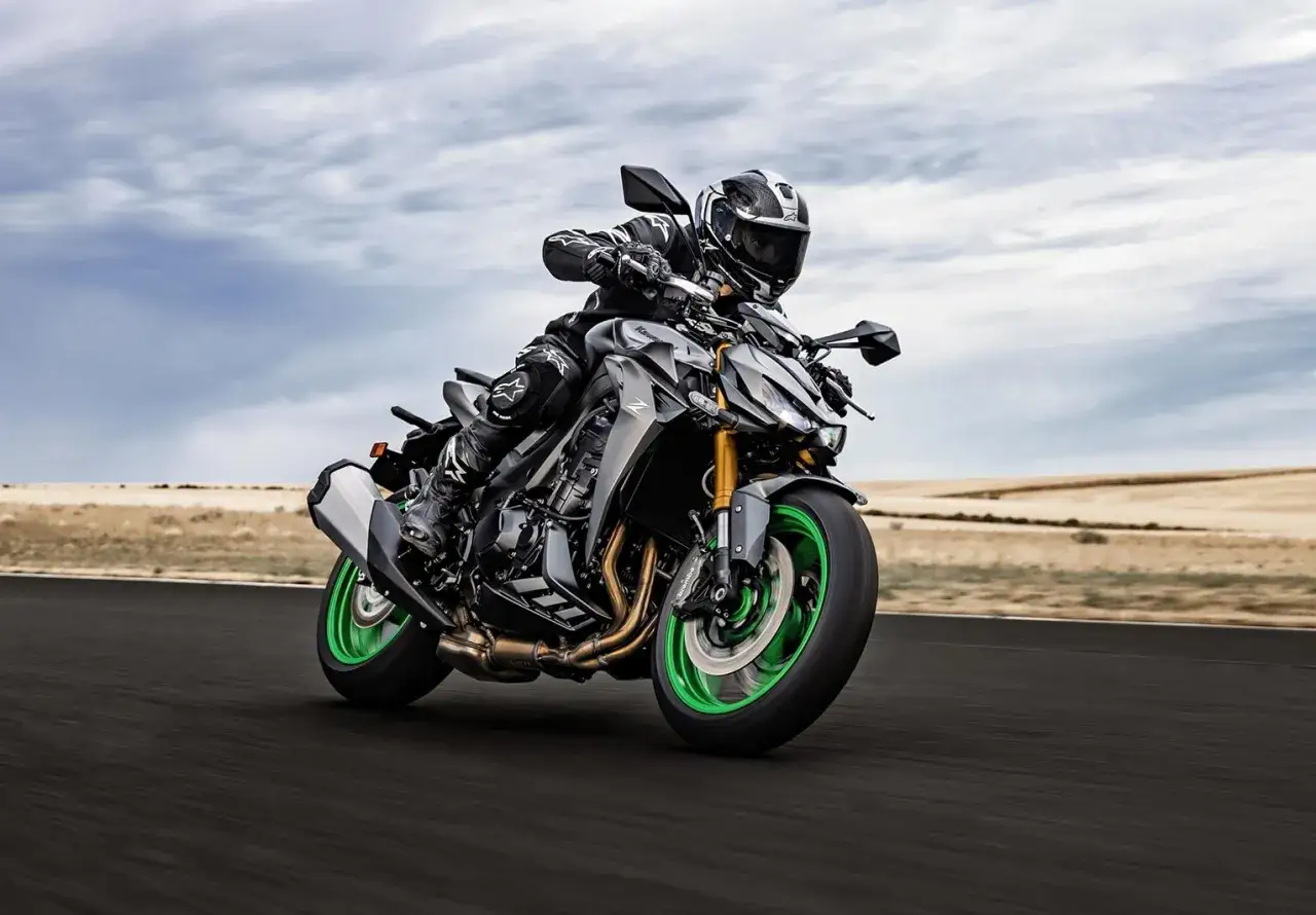 Kawasaki Z1100 grigia con dettagli verdi, guidata da un motociclista in tenuta da gara su una strada deserta.