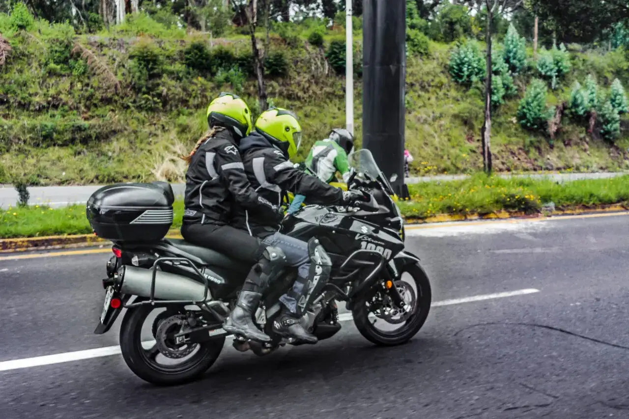 Coppia in moto con abbigliamento tecnico, caschi gialli e giacche nere. Perfetto esempio di come vestirsi per andare in moto passeggero in sicurezza.