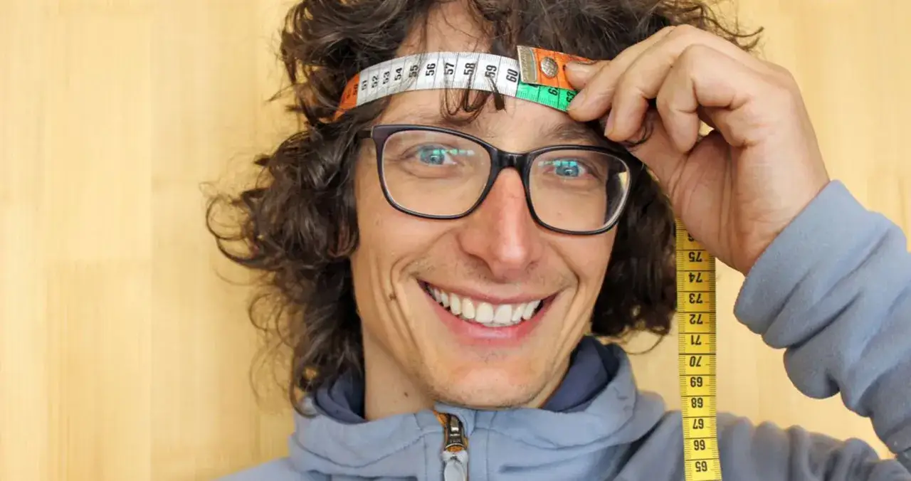 Uomo con capelli ricci e occhiali misura la circonferenza della testa per le misure del casco LS2.