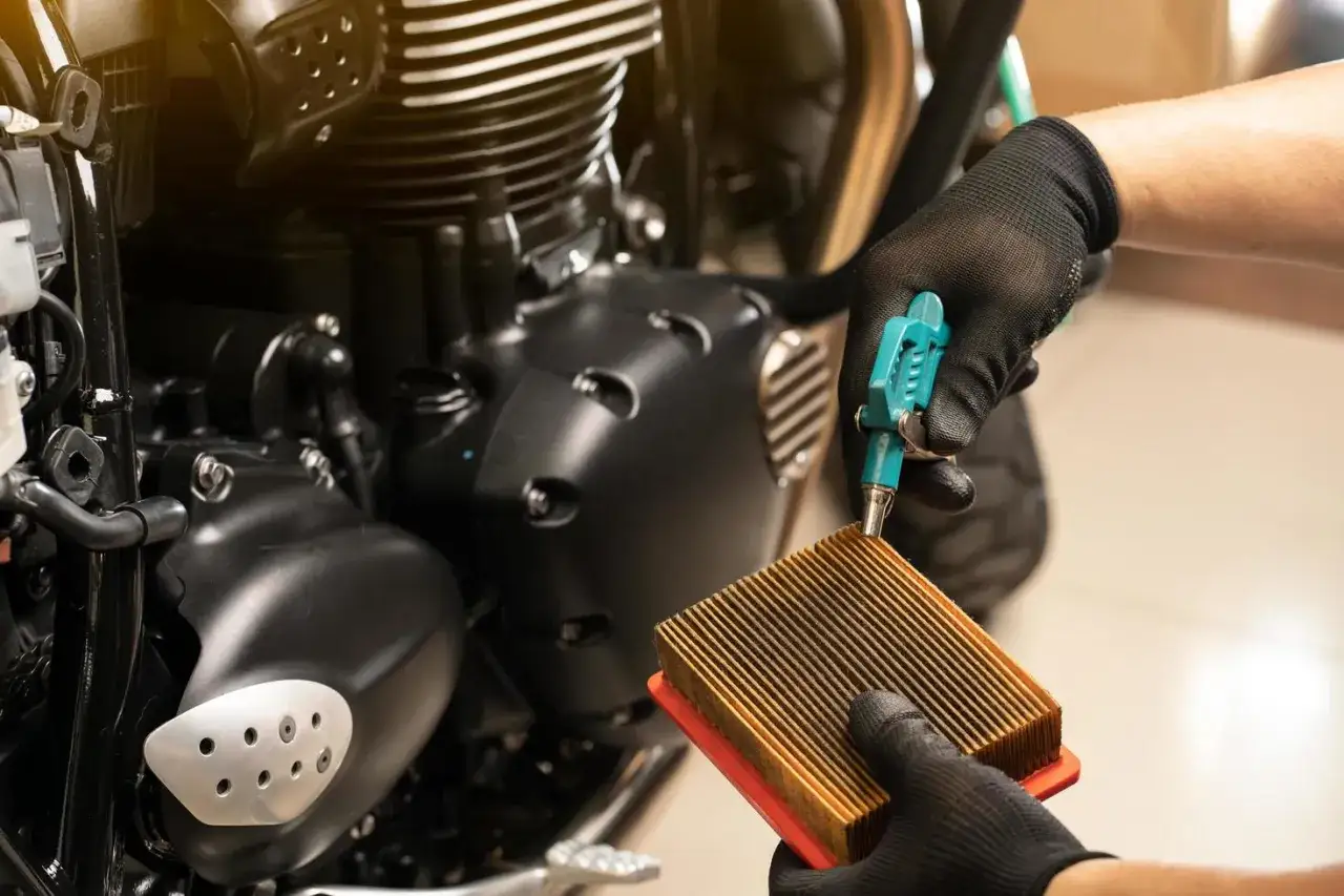 Mani guantate puliscono un filtro aria sporco di moto con un soffiatore.
